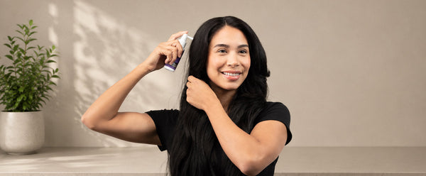 머리카락을 가르고 두피 가까이에 FOLIGAIN TRIOXIDIL 스프레이 도포기를 들고 있는 여성.